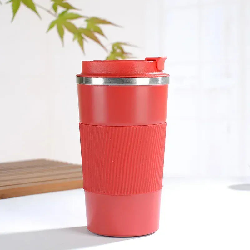 Red travel mug with a silver lid on a white surface with a plant in the background