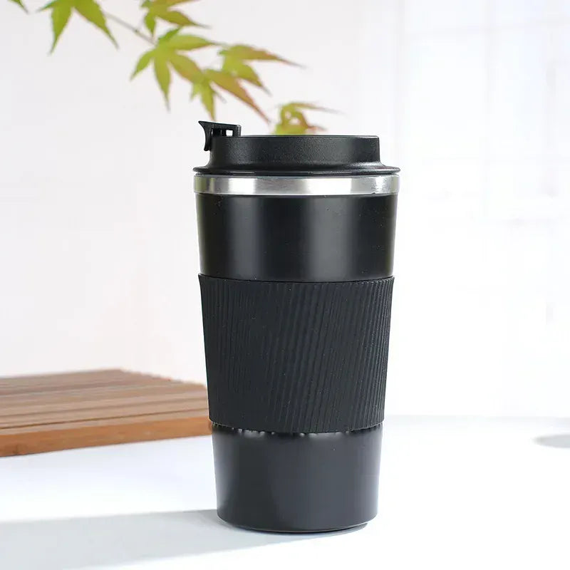 Black insulated travel mug with a bamboo mat and plant in the background