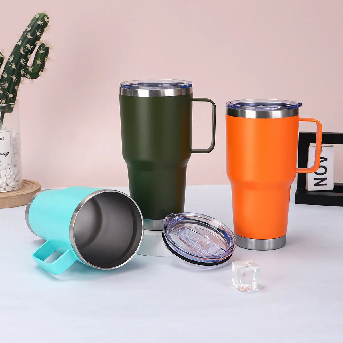 Four colorful insulated travel mugs on a light surface with a cactus plant in the background.