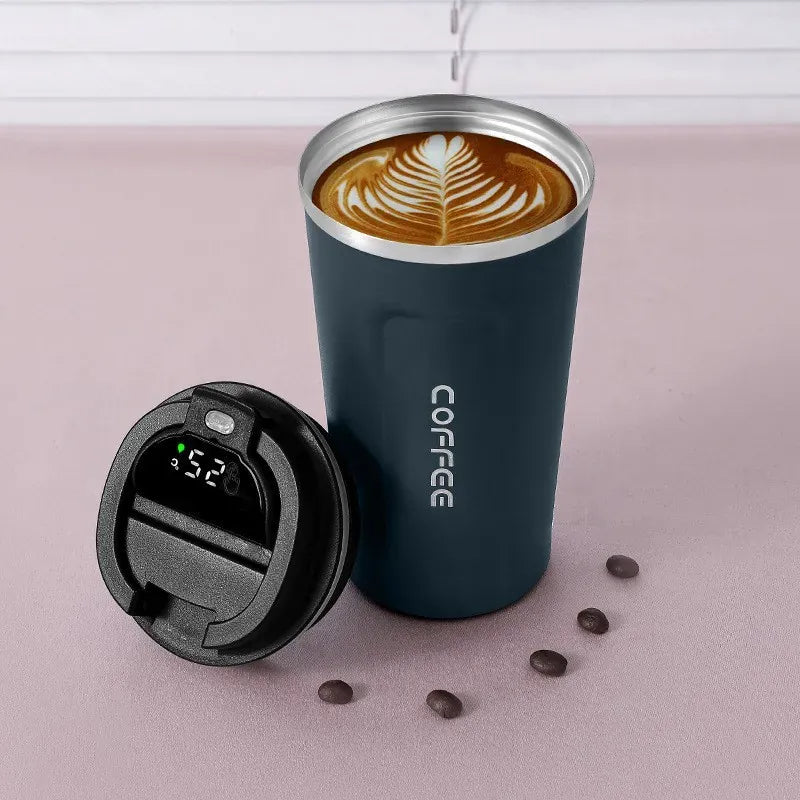 Blue insulated coffee cup with a digital temperature display lid on a pink surface with coffee beans.