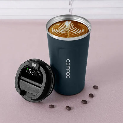 Blue insulated coffee cup with a digital temperature display lid on a pink surface with coffee beans.