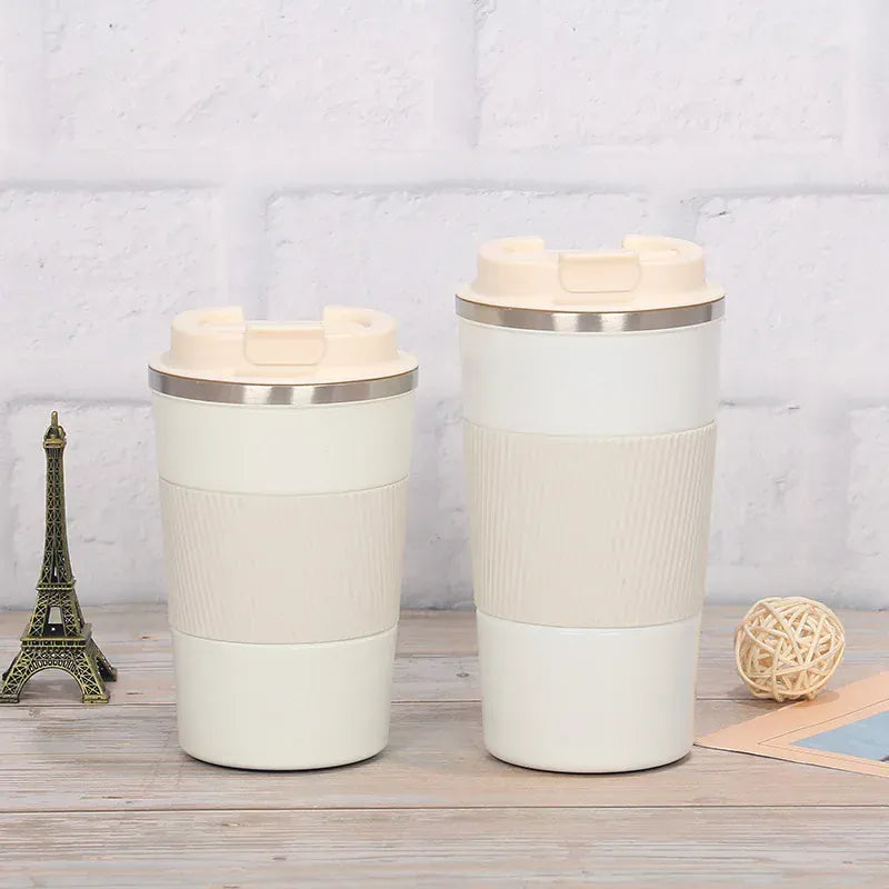 Two white travel mugs with silver lids on a wooden surface with a light gray background.