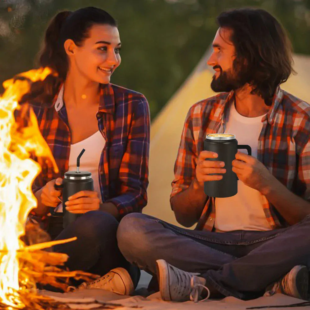 Two people sitting by a campfire, holding insulated mugs.
