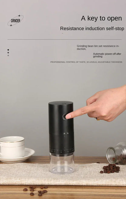 Black coffee grinder with a hand pointing to it, surrounded by coffee beans and a cup on a wooden surface.
