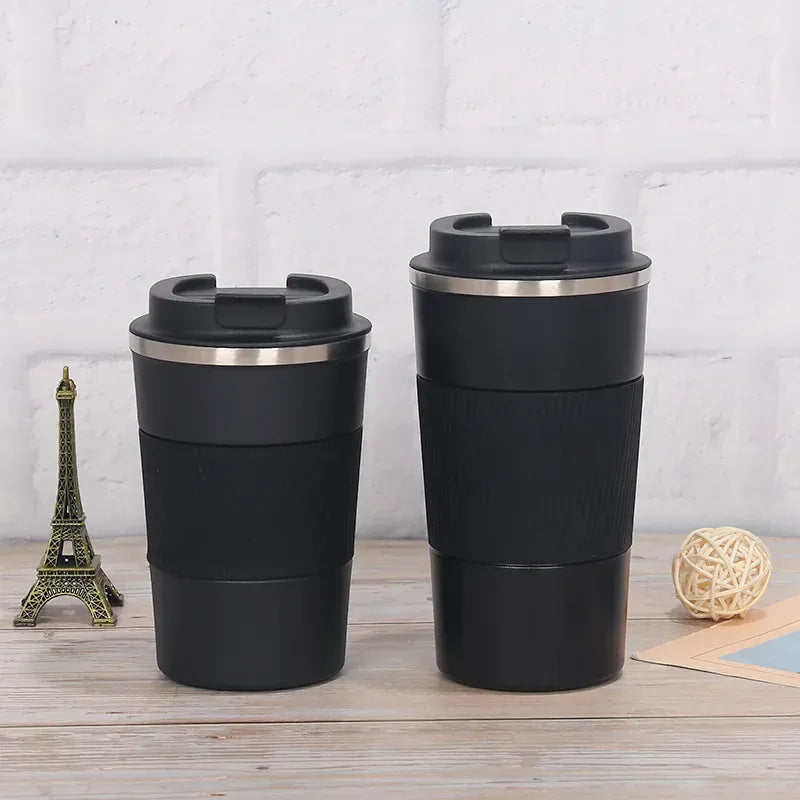 Two black insulated travel mugs with silver lids on a wooden surface with a light gray textured background.