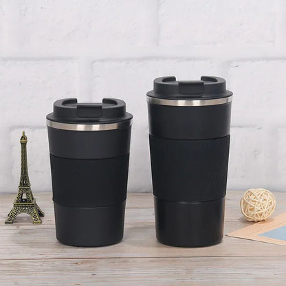 Two black insulated travel mugs with silver lids on a wooden surface with a light gray textured background.