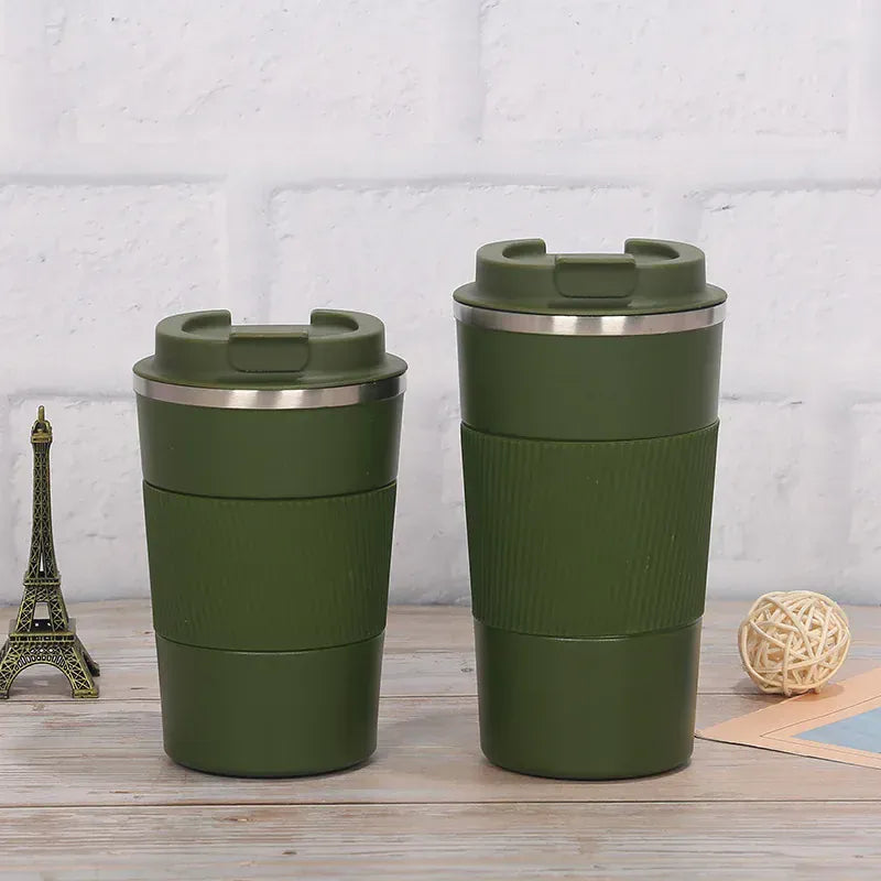 Two green travel mugs with silver lids on a wooden surface with a light gray textured wall background.