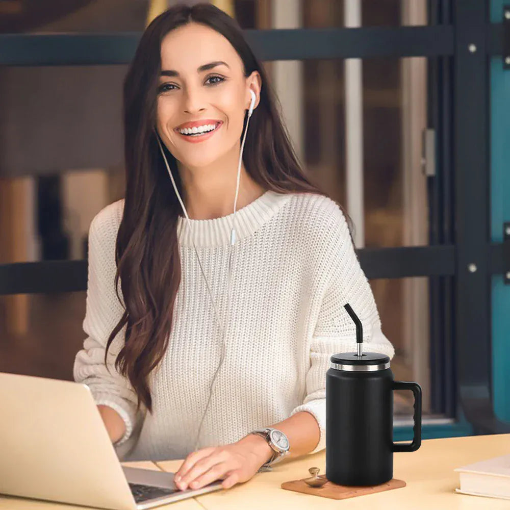 Woman sitting at a desk with a laptop and black mug, wearing earphones.