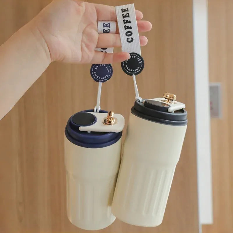 Two white travel mugs with black lids held by a hand against a wooden background.