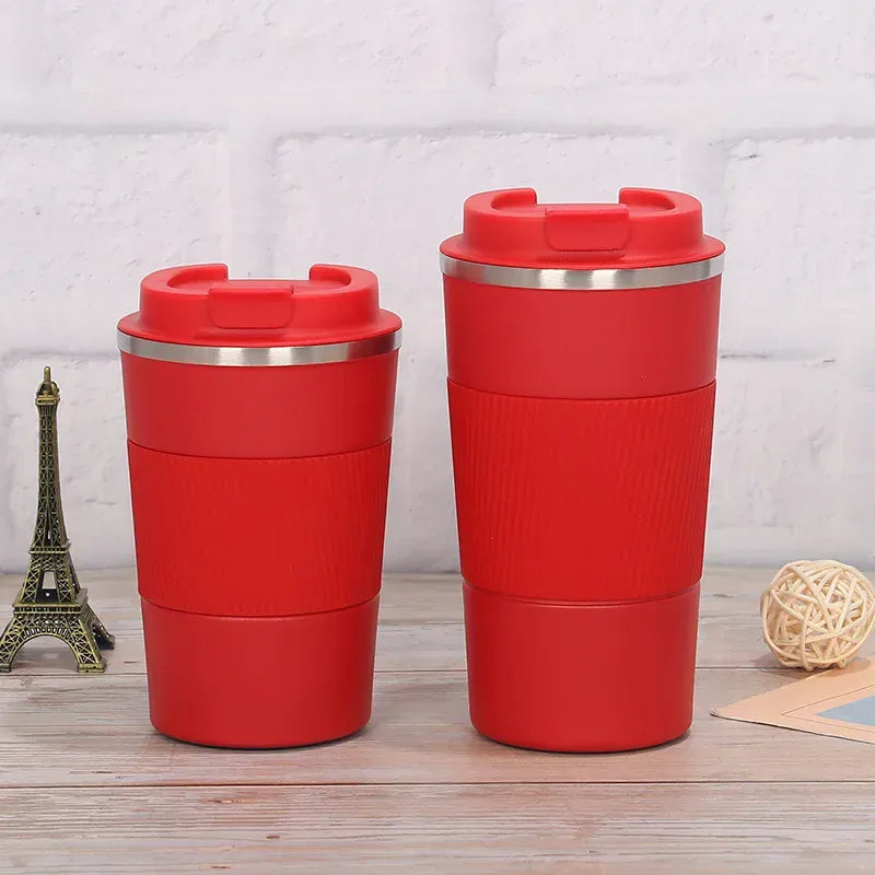 Two red travel mugs with silver lids on a wooden surface with a light gray textured background.