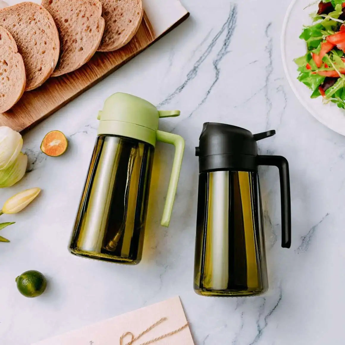 Two olive oil dispensers on a marble surface with bread and salad in the background.