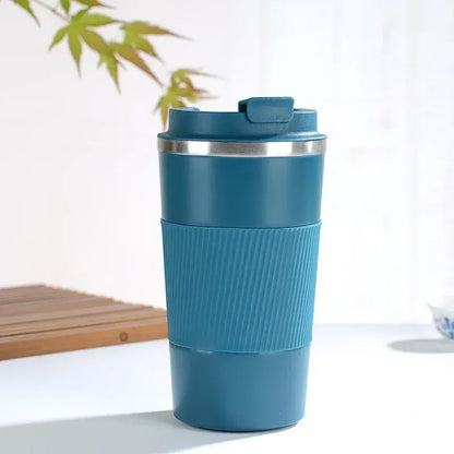 Blue insulated travel mug with a silver lid on a white surface with a plant in the background