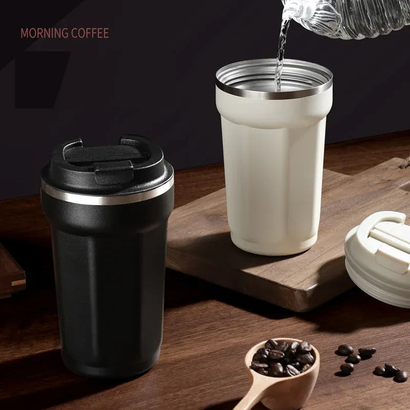 Black and white insulated travel mugs on a wooden surface with coffee beans and a scoop.