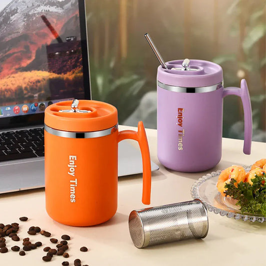 Orange and purple insulated travel mugs with straws on a desk next to a laptop and coffee beans.