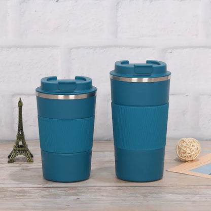 Two blue travel mugs with silver lids on a wooden surface with a light gray brick wall background.