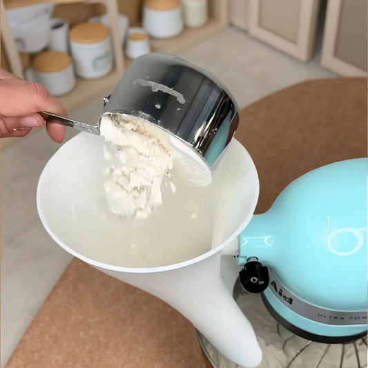 Person using a measuring cup to add ingredients into a kitchen mixer.