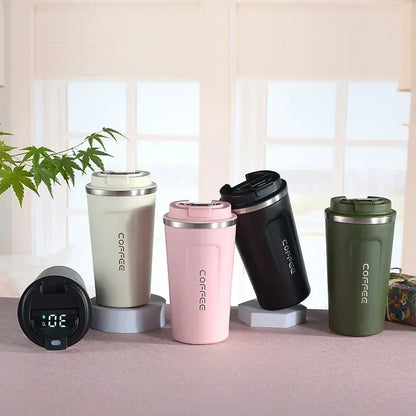 Four insulated coffee tumblers in different colors on a surface with a plant and window in the background.